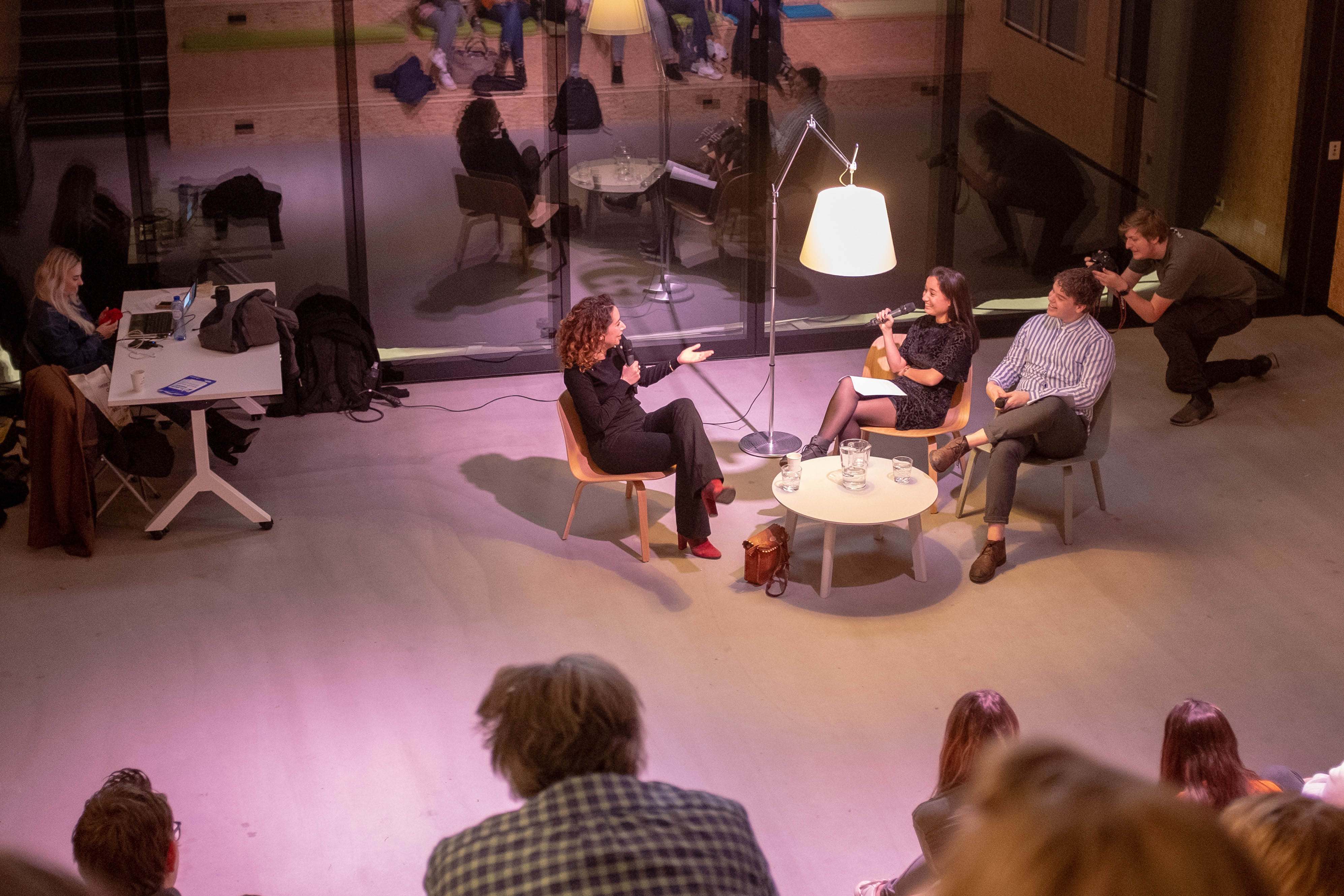 Uitzicht vanaf de oplopende collegebanken naar het panelgesprek tussen 3 journalisten voorin de zaal